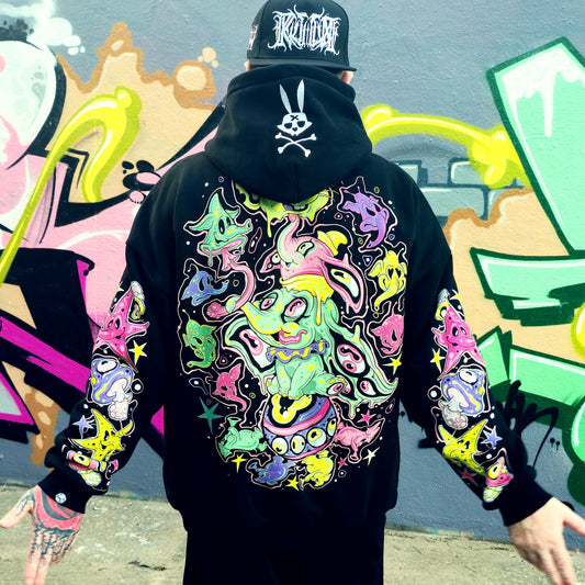 Person wearing a black hoodie with colorful abstract designs in front of a graffiti wall.