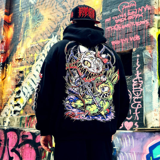 Person wearing a black hoodie with a colorful graphic design in front of a graffiti-covered wall.
