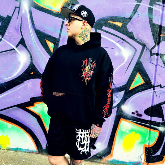 Person wearing a black hoodie with a graphic design in front of a colorful graffiti wall.