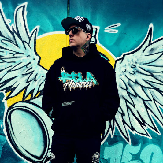Person wearing a black hoodie with 'Alpha Apparel' logo in front of a colorful mural with wings.