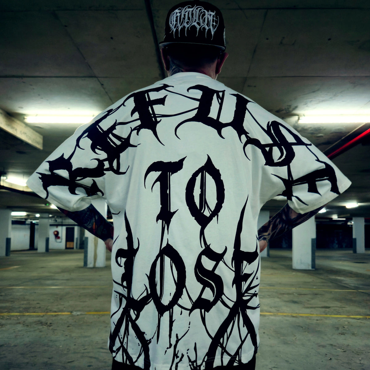 Person wearing a white t-shirt with black text in an underground parking lot