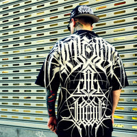 Person wearing a black and white patterned shirt with a cap, standing in front of a metallic shutter.