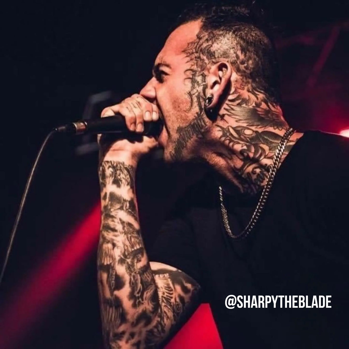Person with tattoos holding a microphone against a dark background