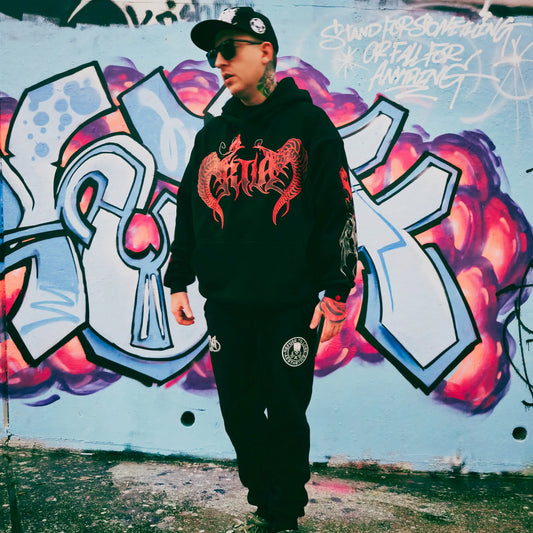 A person wearing a black hoodie with 'RTLA' and a graphic design, standing in front of a graffiti-covered wall.
