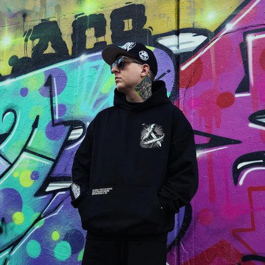 Person wearing a black hoodie with a logo in front of colourful graffiti art. RTLA-Apparel