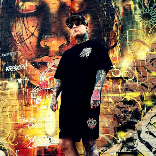 Person wearing a black t-shirt with a logo in front of a colorful graffiti wall.
