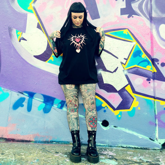 Person wearing a black oversized shirt with a graphic design, standing in front of colorful graffiti.