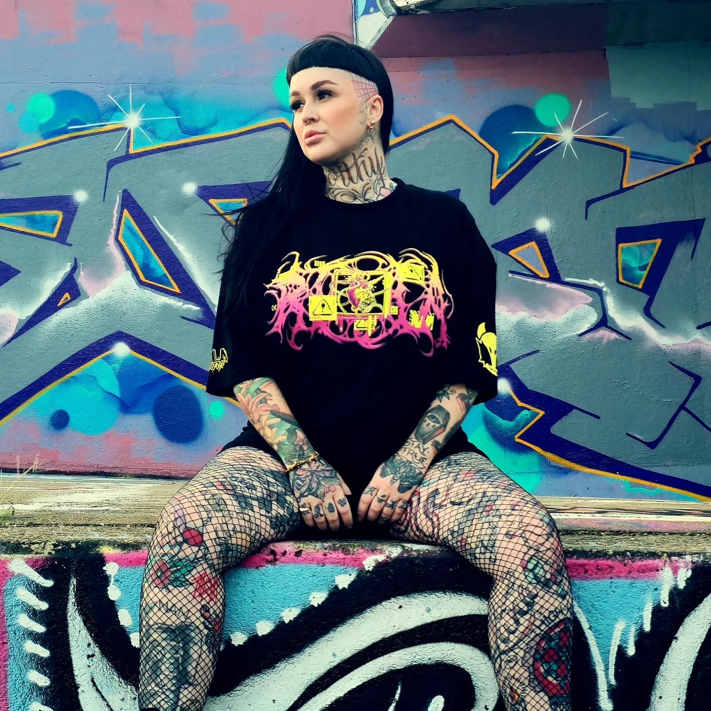 Person with tattoos sitting on a graffiti-covered wall