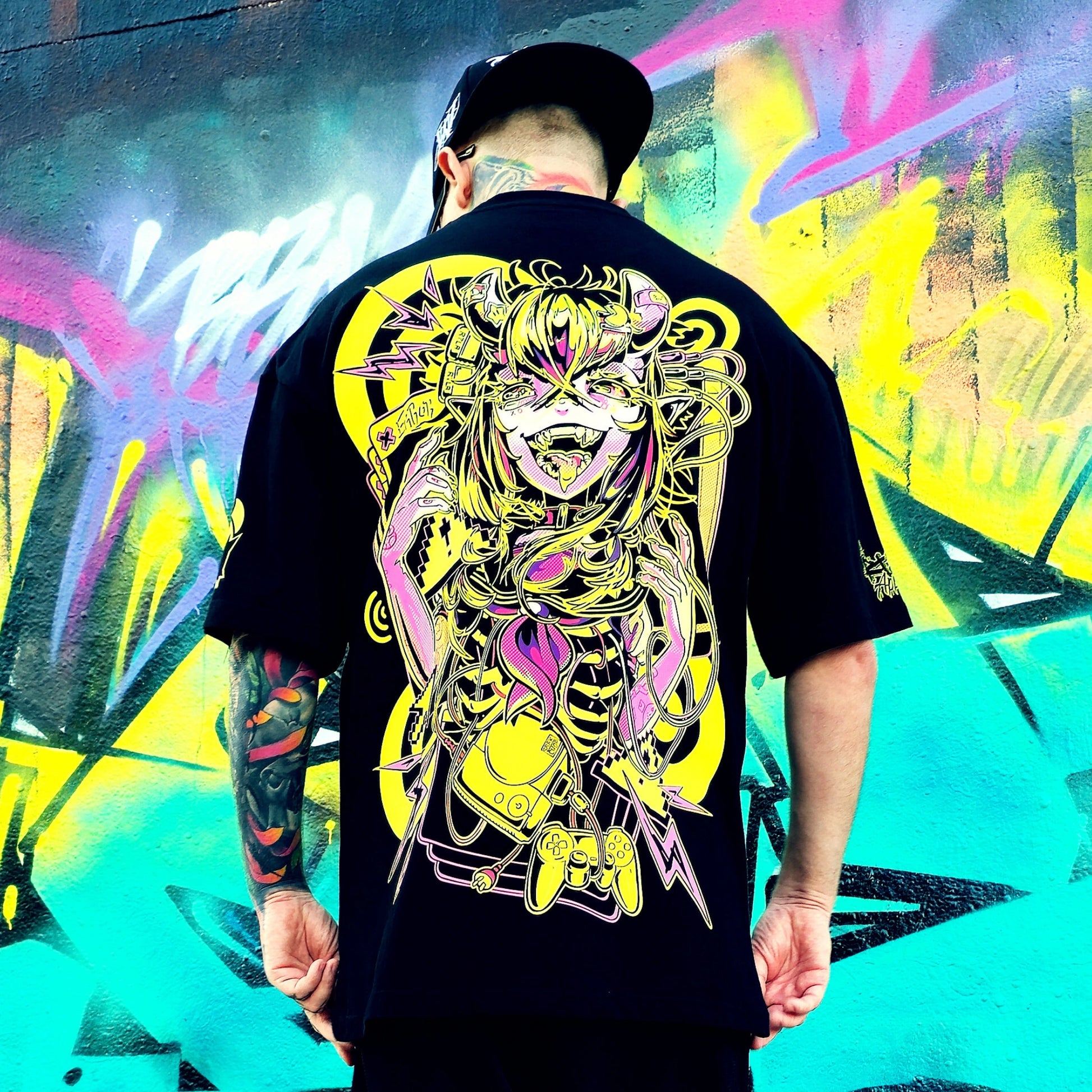 Person wearing a black t-shirt with a colorful graphic design in front of a vibrant graffiti wall.