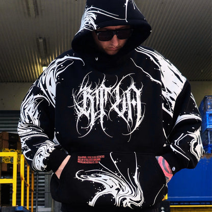 Person wearing a black hoodie with white designs and text, standing in an industrial setting.