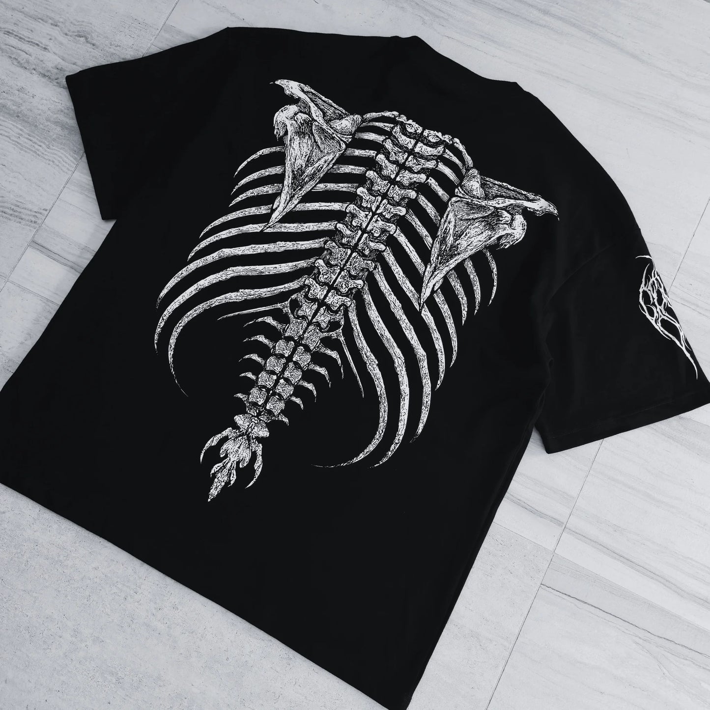 Black t-shirt with a detailed skeleton design on a light wooden floor.