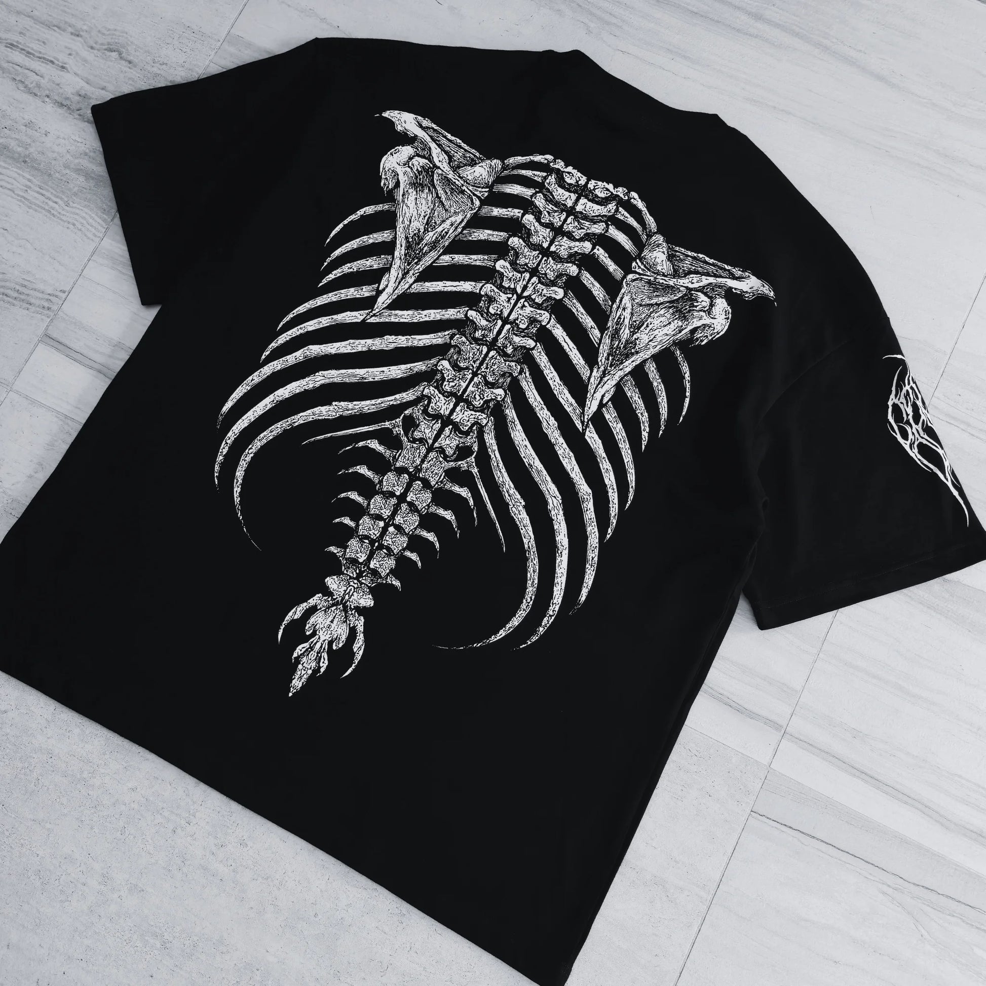 Black t-shirt with a detailed skeleton design on a light wooden floor.