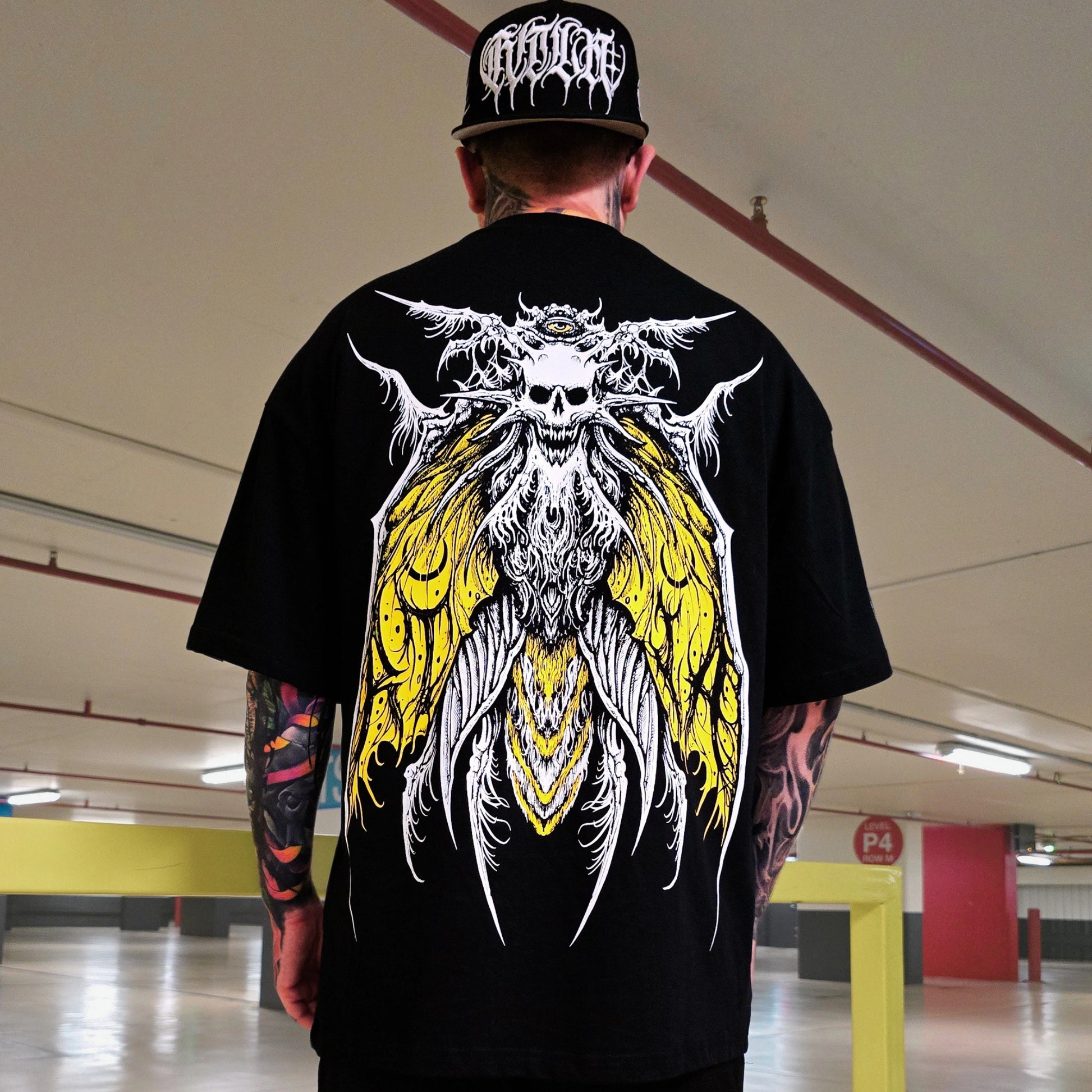 Person wearing a black t-shirt with a white and yellow graphic design in an indoor setting.