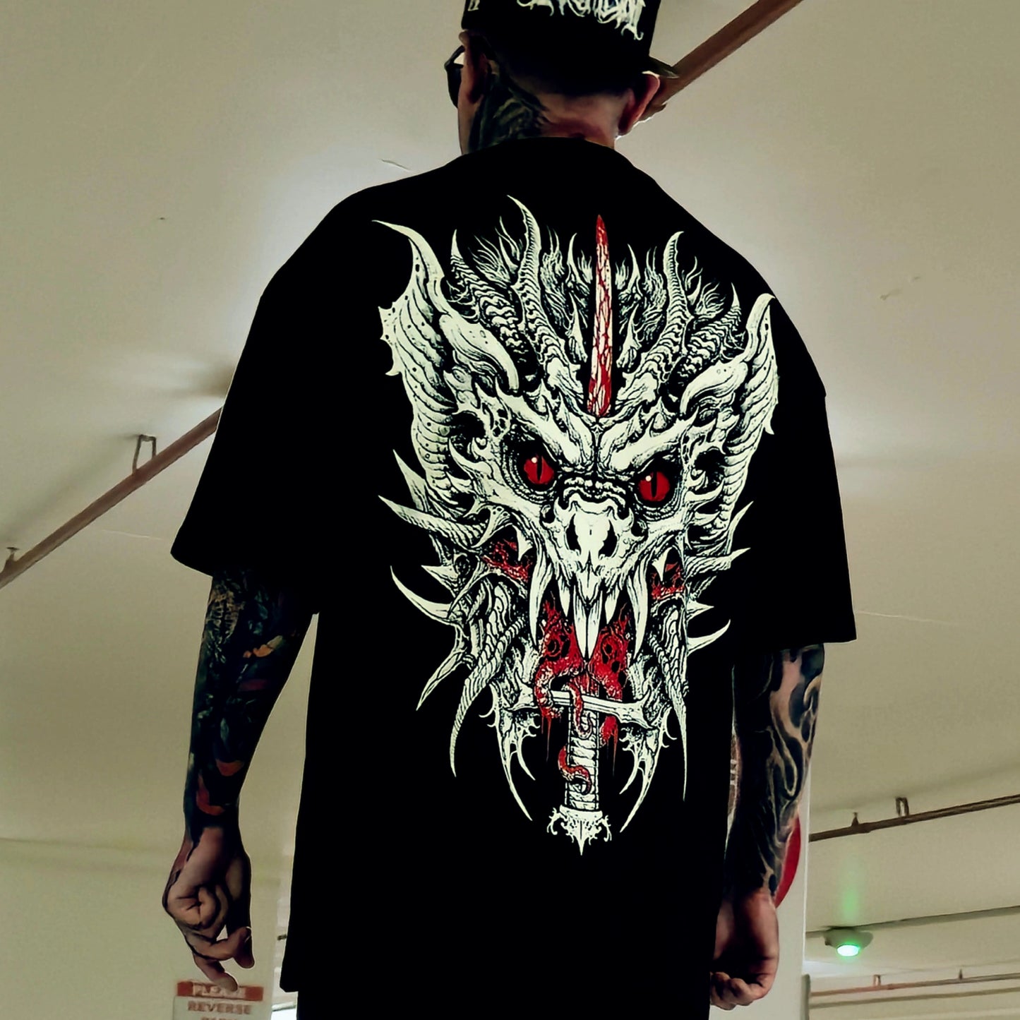 Person wearing a black t-shirt with a dragon design on the back, standing indoors.