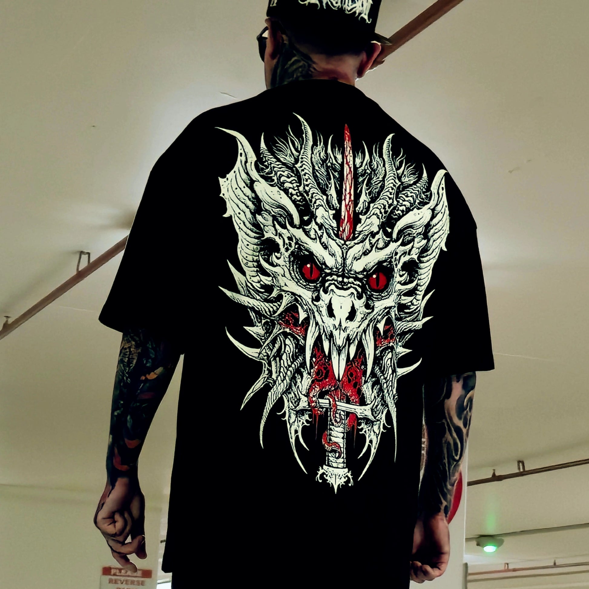 Person wearing a black t-shirt with a dragon design on the back, standing indoors.