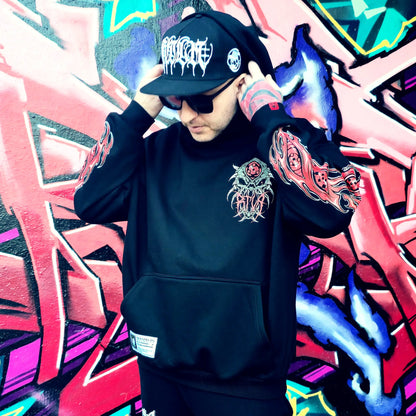 Person wearing a black hoodie with a floral design and a cap in front of colourful graffiti. RTLA-Apparel
