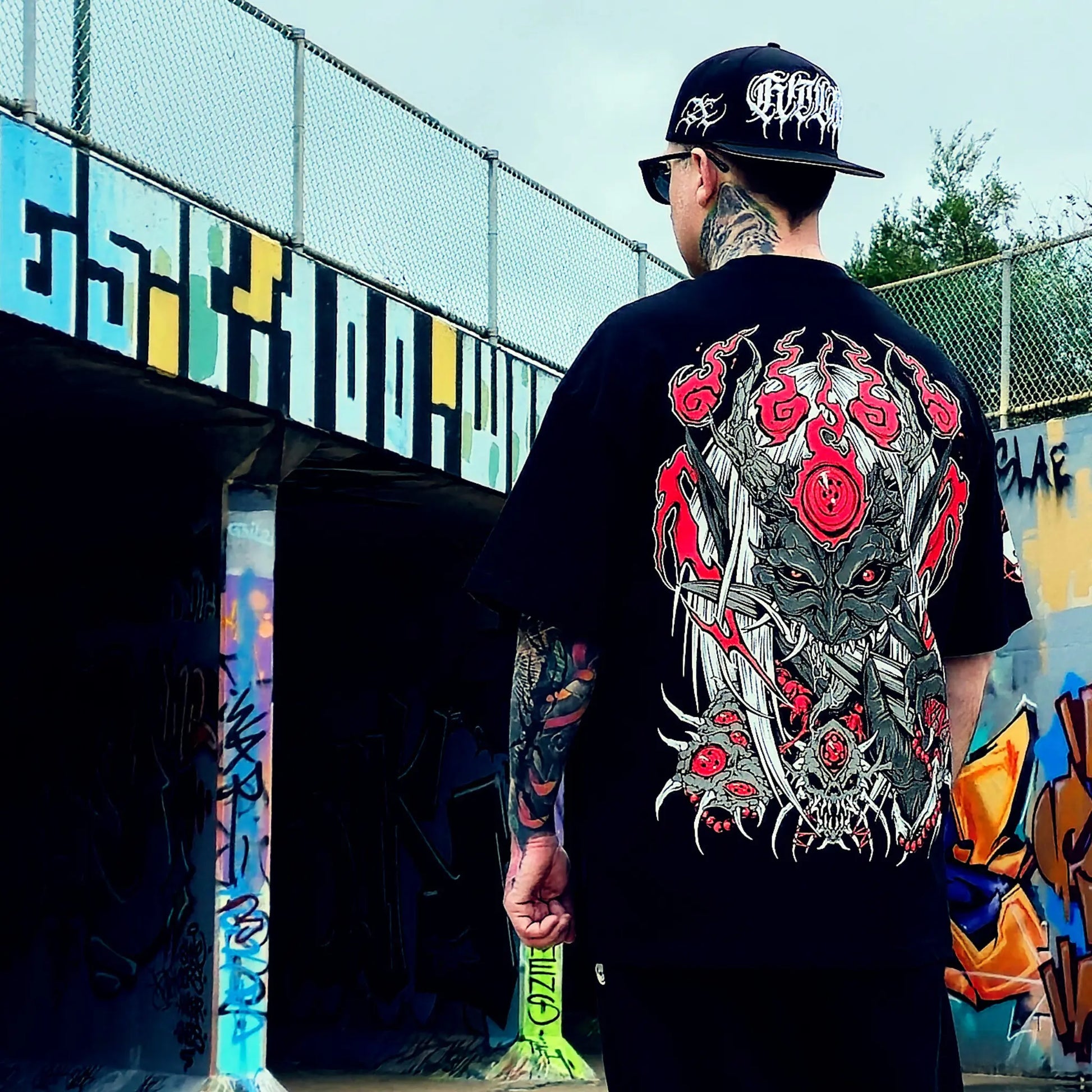 Person wearing a black t-shirt with a detailed graphic design, standing in front of a colorful mural.