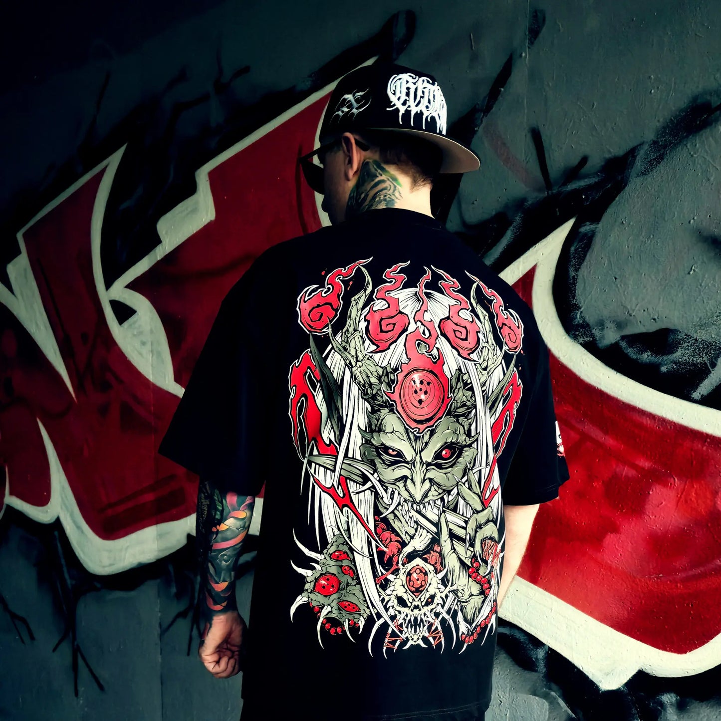 Person wearing a black t-shirt with a colorful graphic design, standing in front of a red and white flag.