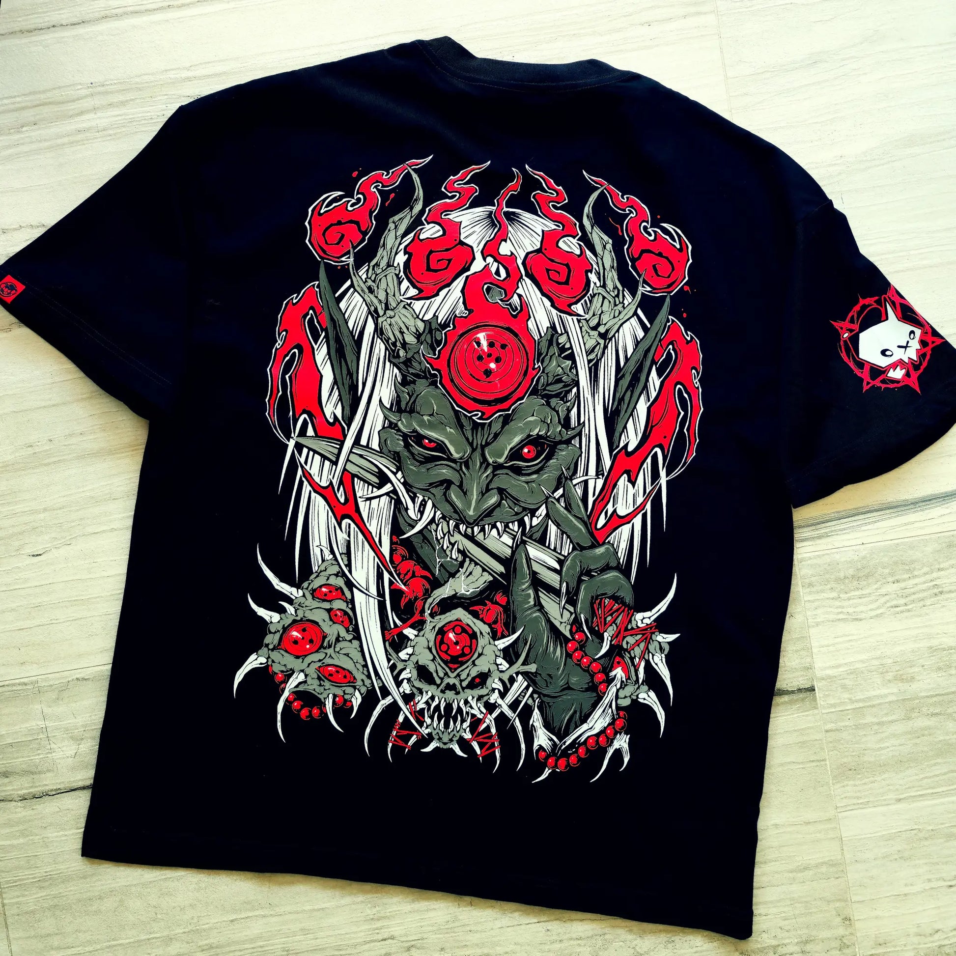 Black t-shirt with a graphic design of a creature with red eyes and red flowers on a wooden surface.