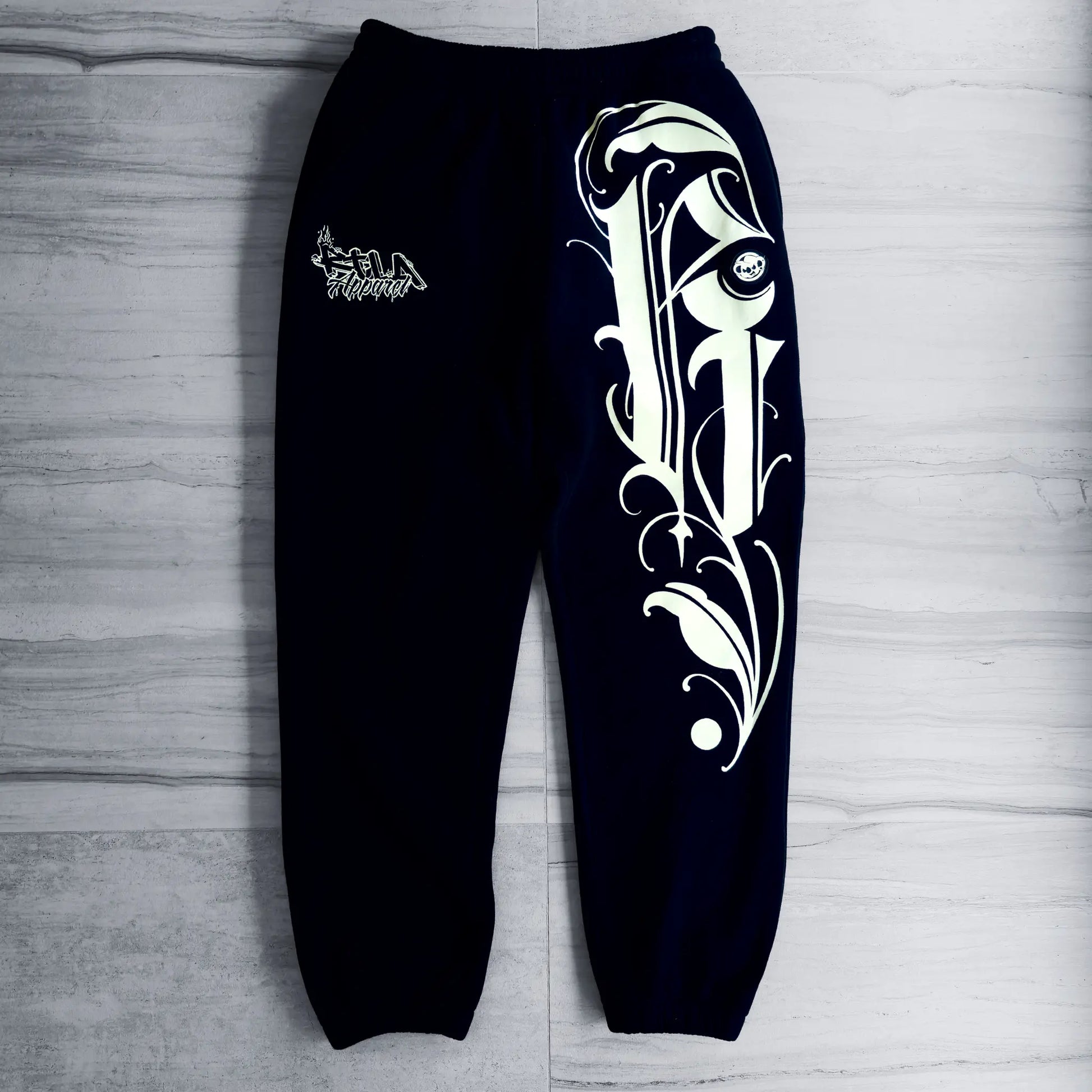 Black sweatpants with white tribal design on a gray wooden surface