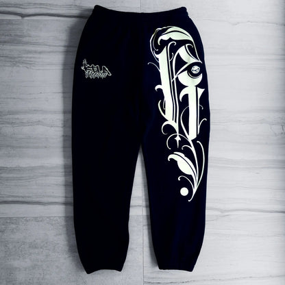 Black sweatpants with white tribal design on a gray wooden surface