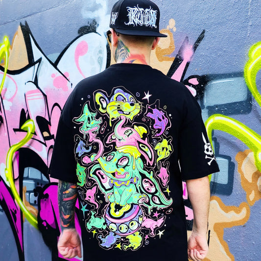 Person wearing a black t-shirt with colorful graphic design in front of a graffiti wall.
