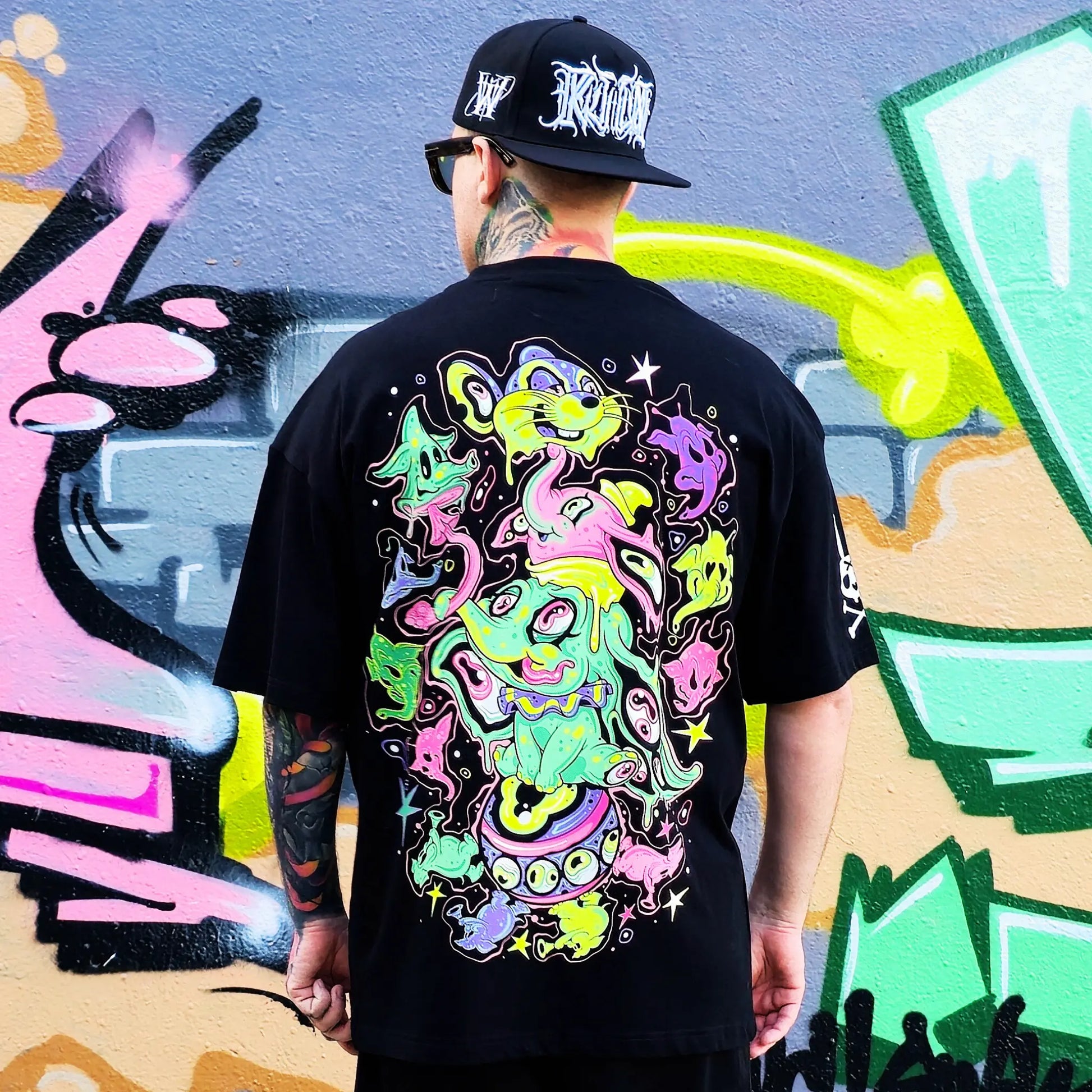 Person wearing a black t-shirt with colorful abstract design in front of graffiti art.