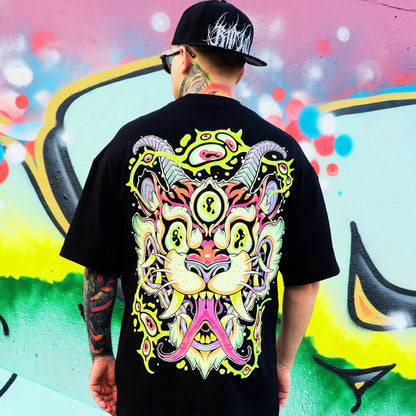 Person wearing a black t-shirt with a colorful graphic design, standing in front of a vibrant graffiti wall.