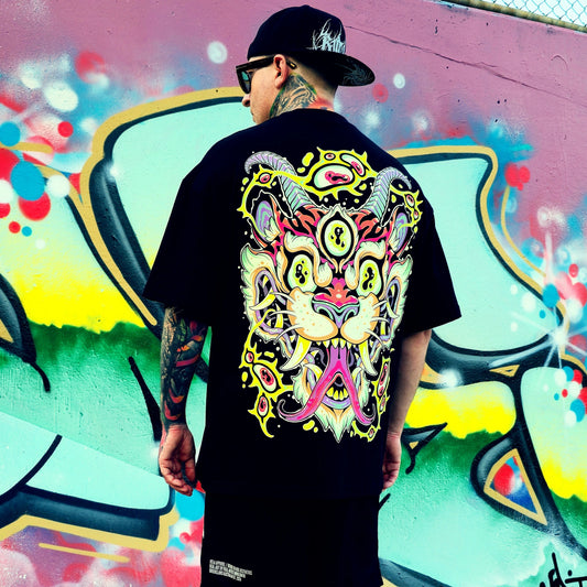 Person wearing a black t-shirt with a colorful graphic design, standing in front of a vibrant graffiti wall.