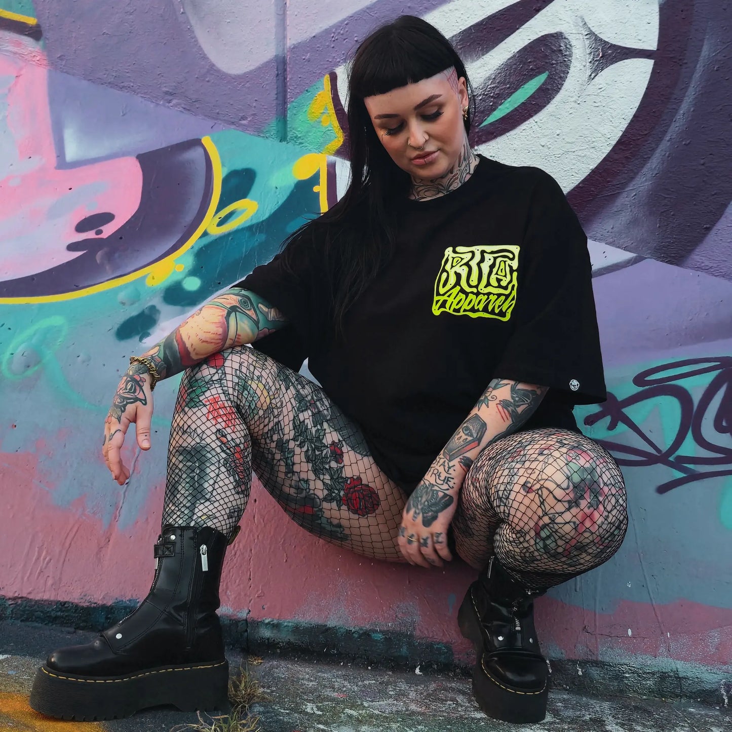 Person with tattoos sitting against a colorful graffiti wall