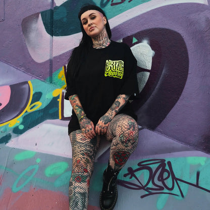 Person with tattoos sitting against a colorful graffiti wall