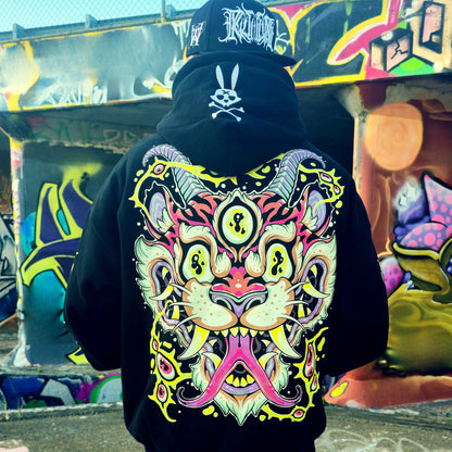 Person wearing a black hoodie with a colorful cat mask design in front of graffiti art.