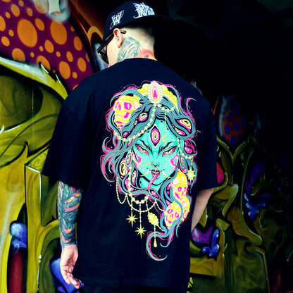 Person wearing a black t-shirt with a colorful graphic design, standing in front of a vibrant graffiti wall.