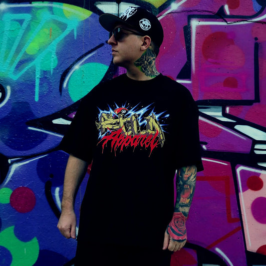 Person wearing a black t-shirt with colourful graphics in front of a vibrant graffiti wall. RTLA-Apparel