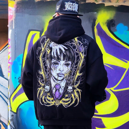 Person wearing a black hoodie with a graphic design, standing in front of colorful graffiti.