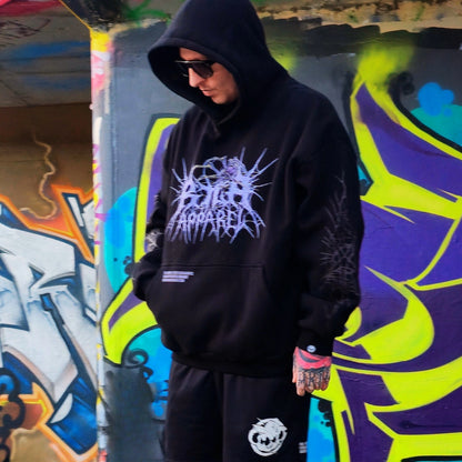 Person wearing a black hoodie with a graphic design in front of colorful graffiti.