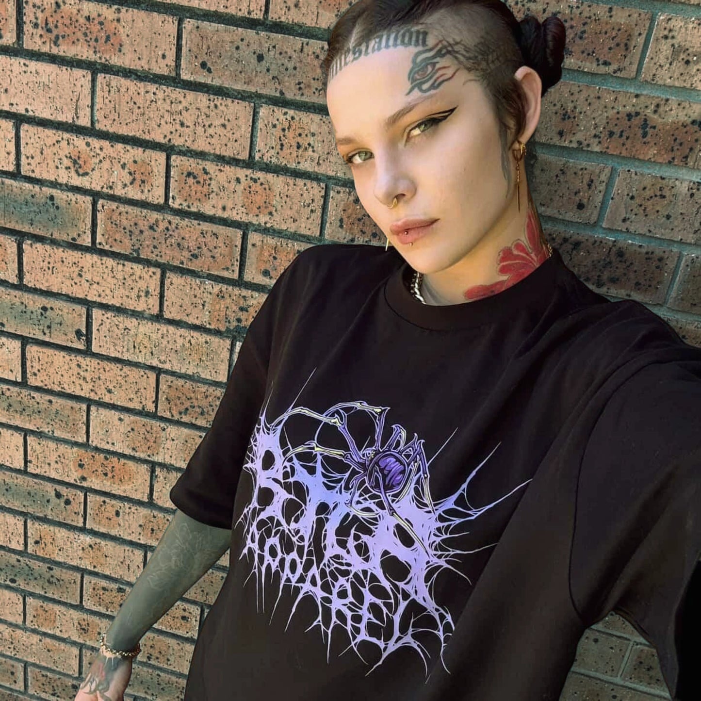 Person wearing a black t-shirt with a purple graphic design against a brick wall.