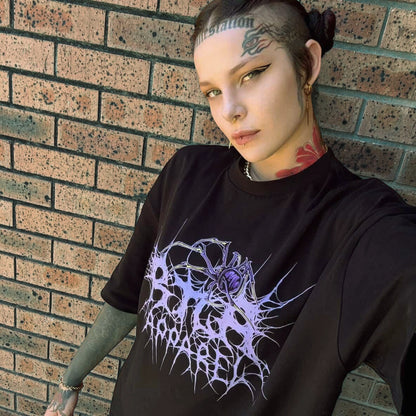 Person wearing a black t-shirt with a purple graphic design against a brick wall.