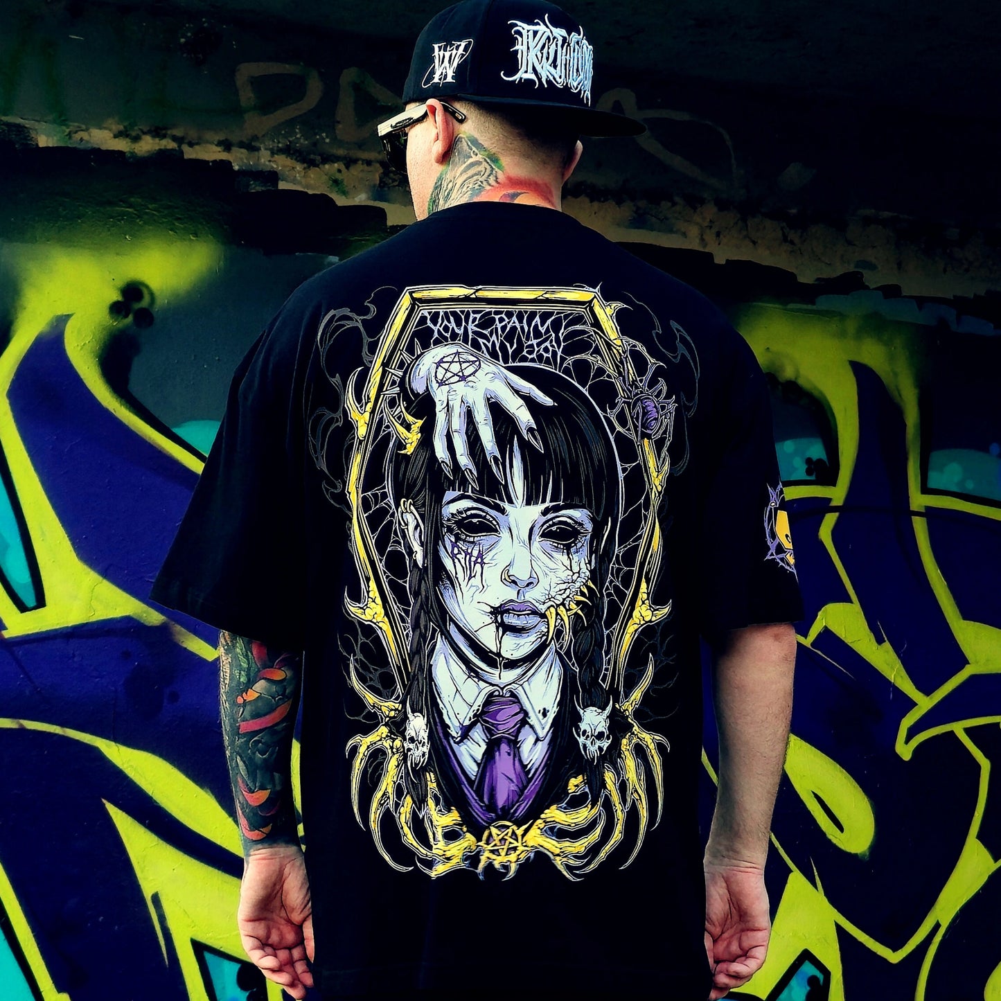 Person wearing a black t-shirt with a graphic design of a woman's face and text, standing in front of a colorful graffiti wall.