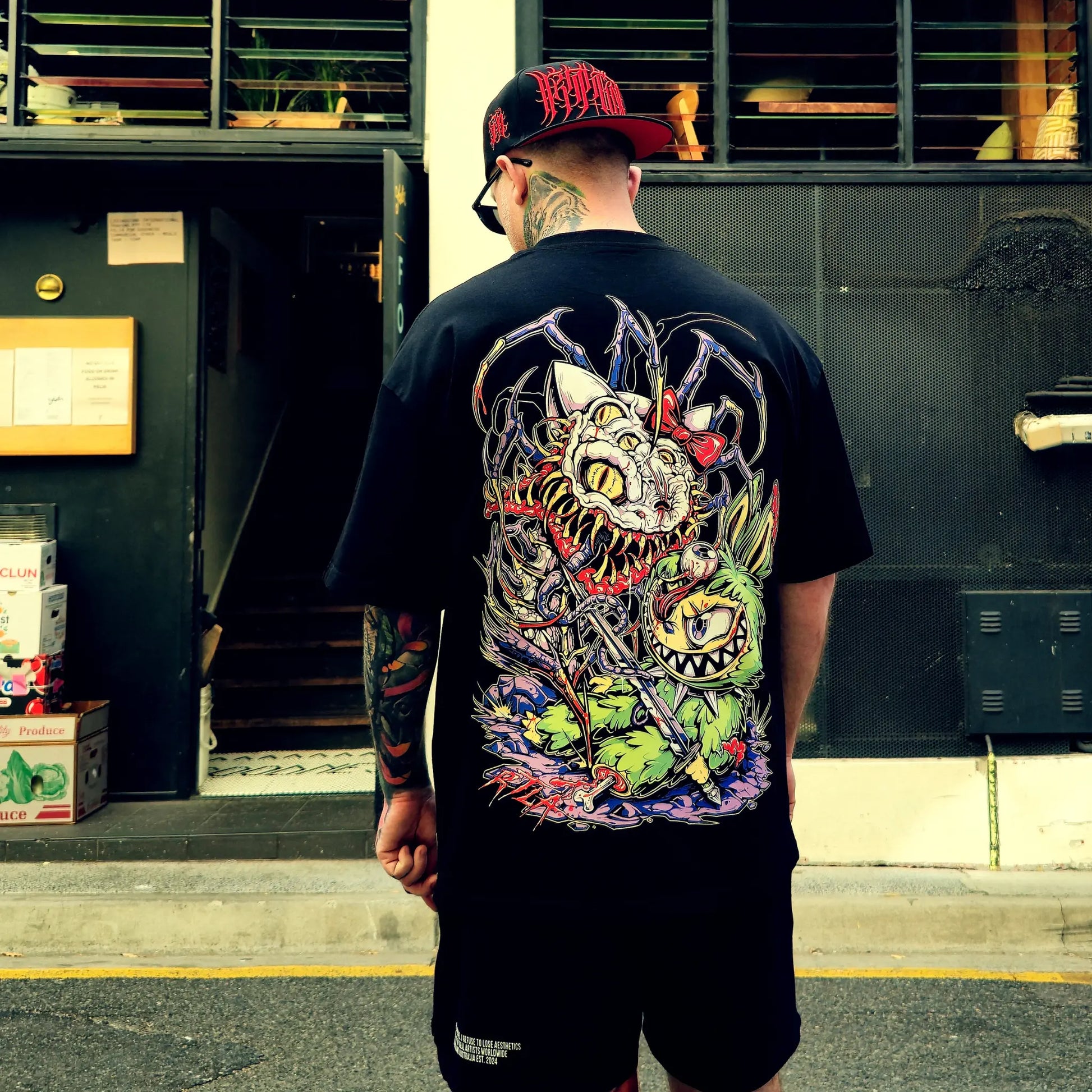 Man wearing a black t-shirt with a colorful graphic design, standing in front of a building entrance.