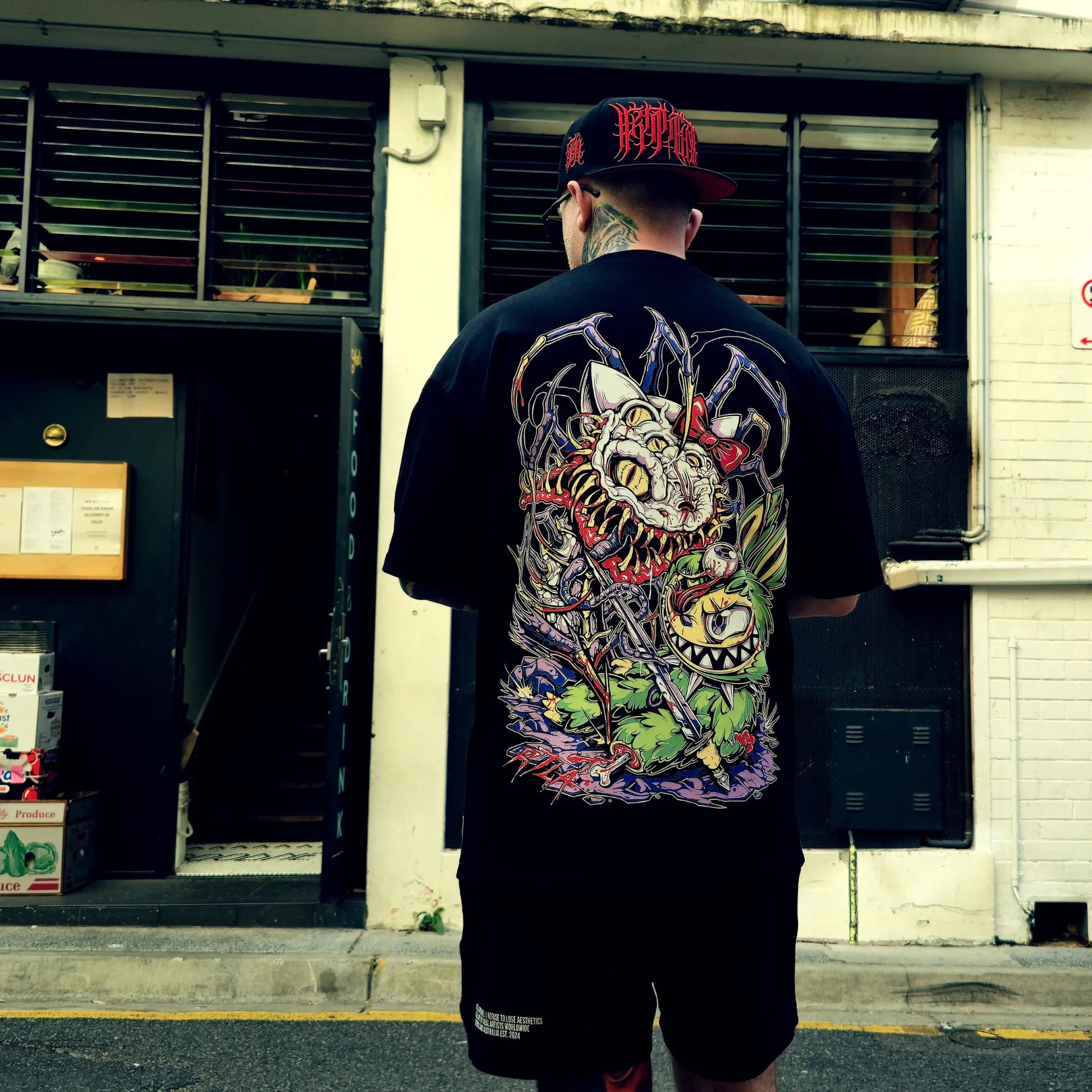 Person wearing a black t-shirt with a colorful graphic design on the back, standing in front of a building.