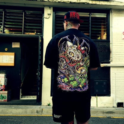 Person wearing a black t-shirt with a colorful graphic design on the back, standing in front of a building.