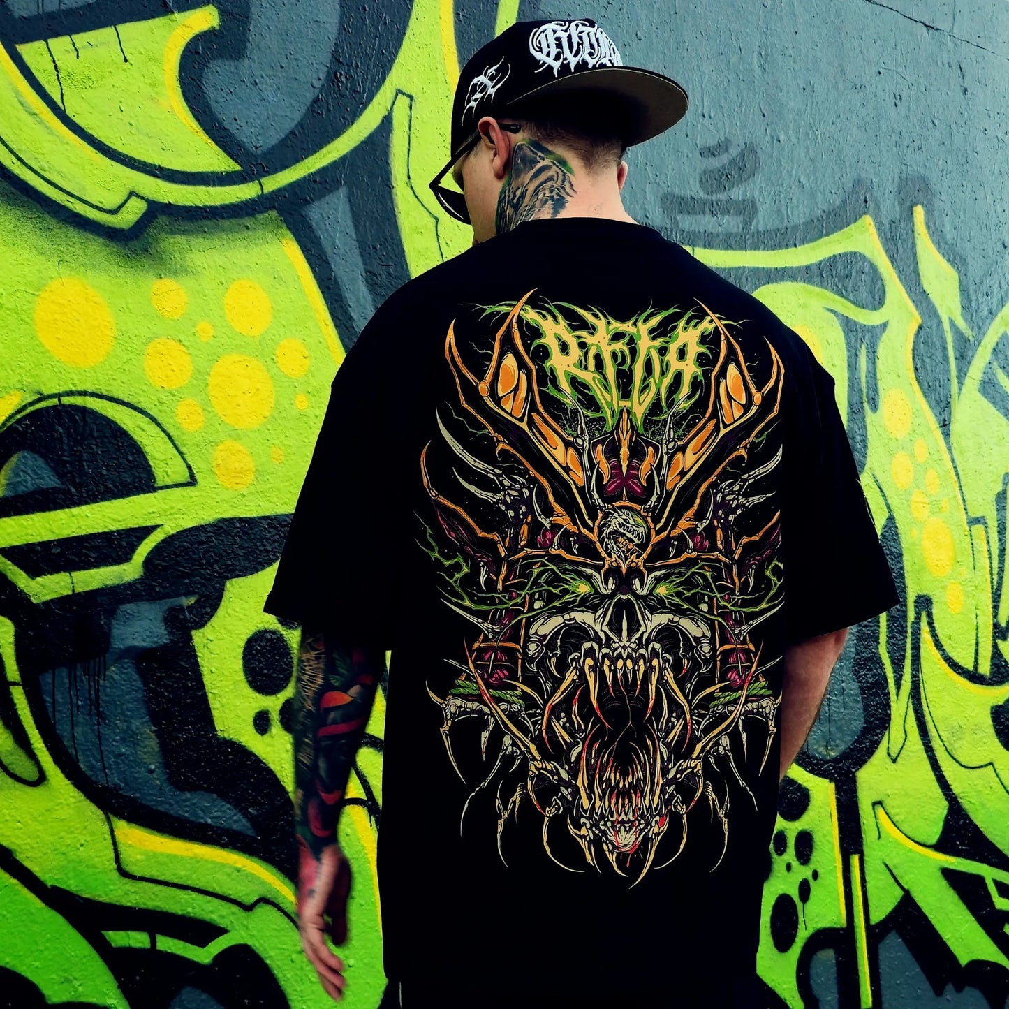 Person wearing a black t-shirt with a colourful dragon design in front of a graffiti wall. RTLA-Apparel