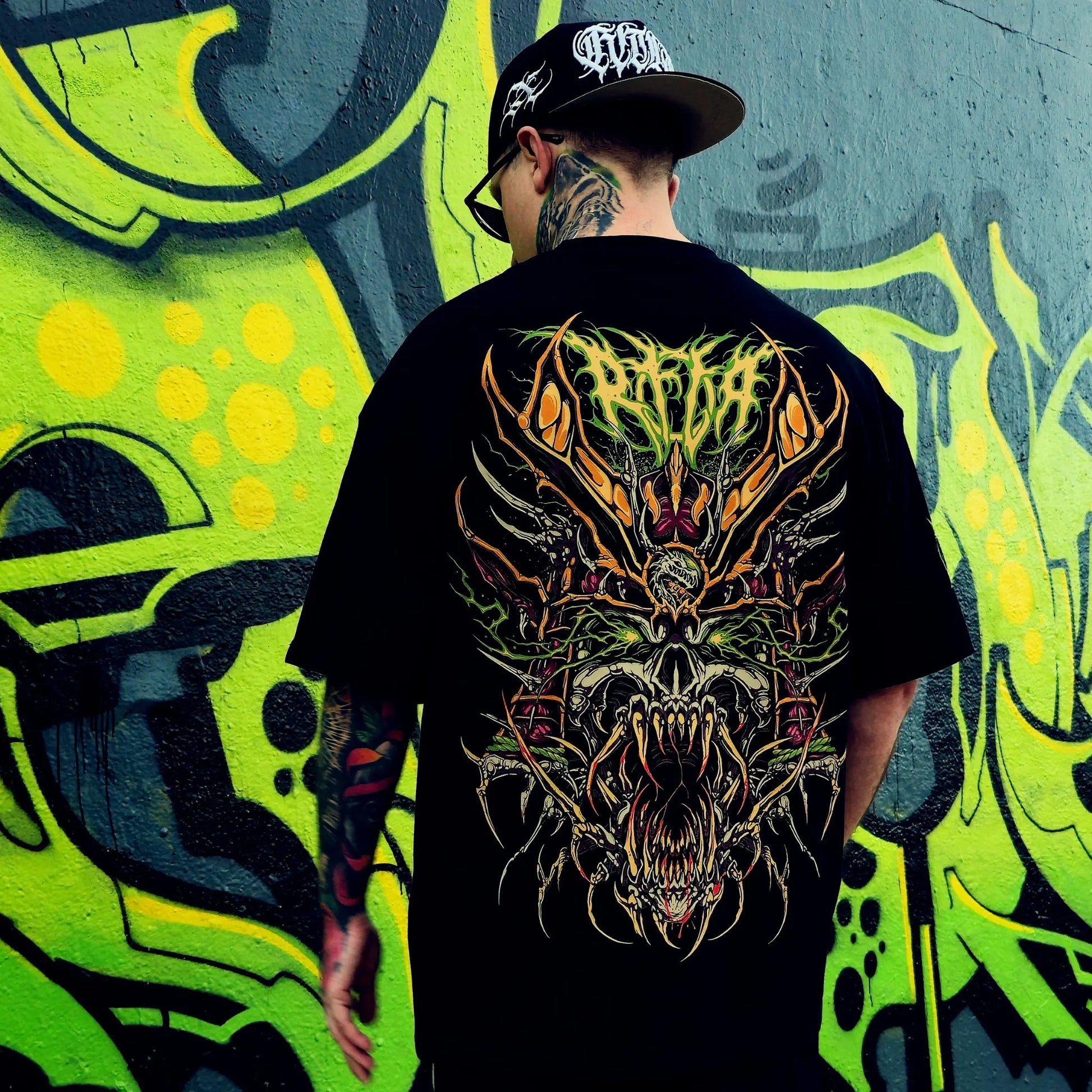 Person wearing a black t-shirt with a colourful dragon design in front of a graffiti wall. RTLA-Apparel
