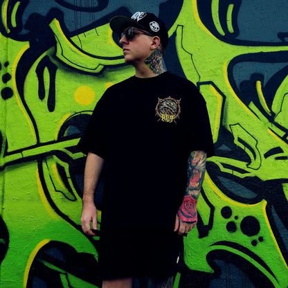 Person wearing a black t-shirt with a logo in front of a vibrant graffiti wall. RTLA-Apparel