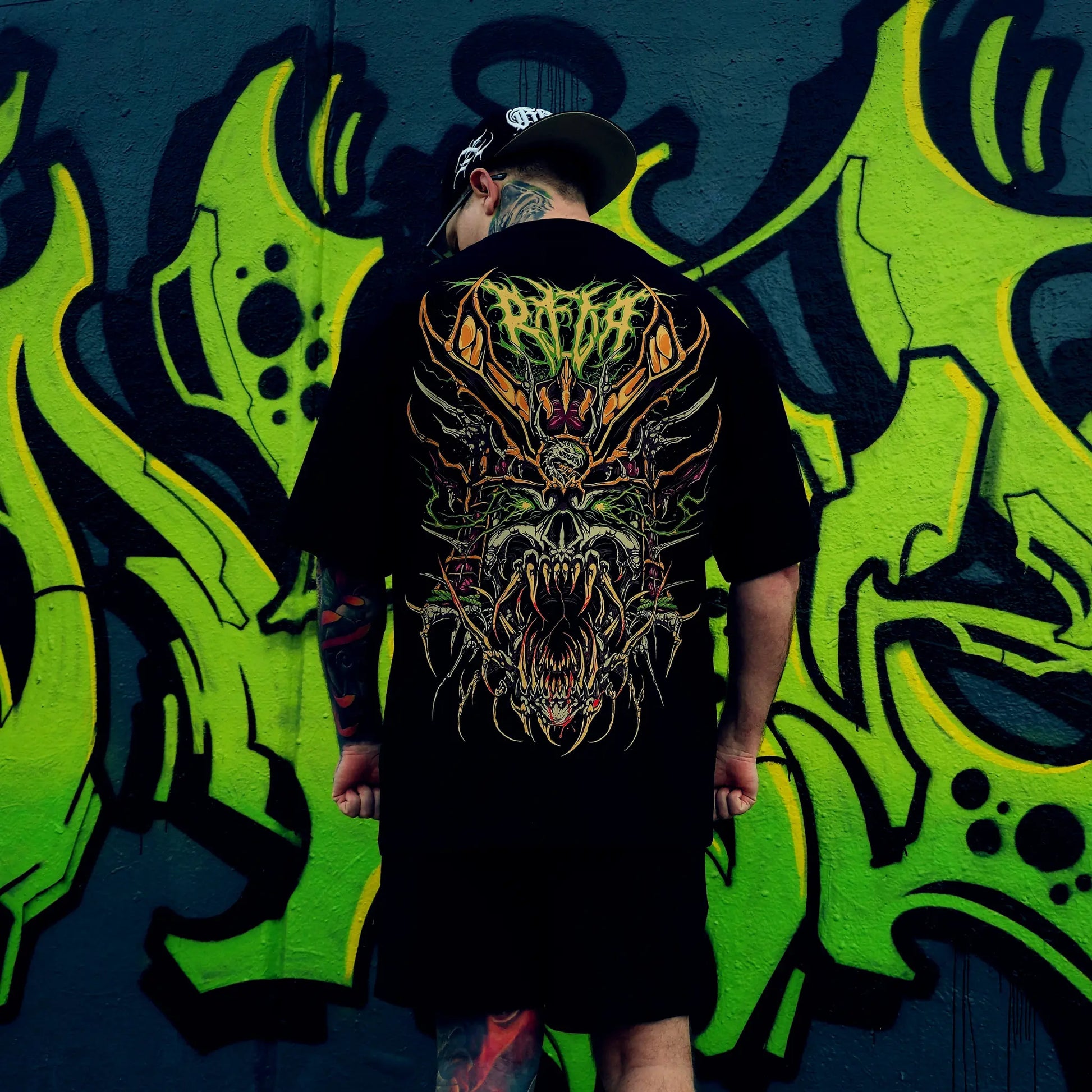 Person wearing a black t-shirt with a colourful graphic design in front of a vibrant graffiti wall. RTLA-Apparel
