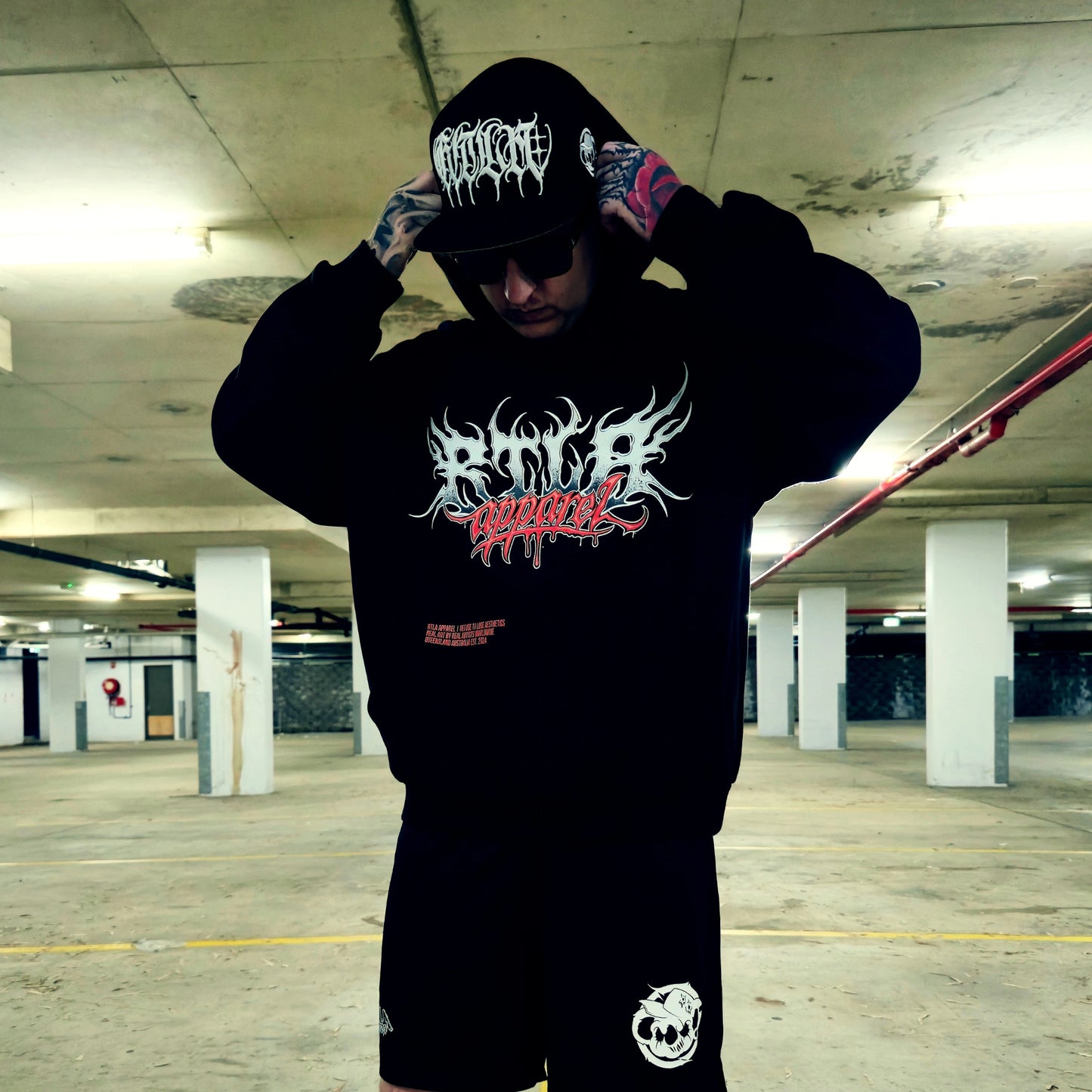 Person wearing a black hoodie with graphic designs in an underground parking lot.