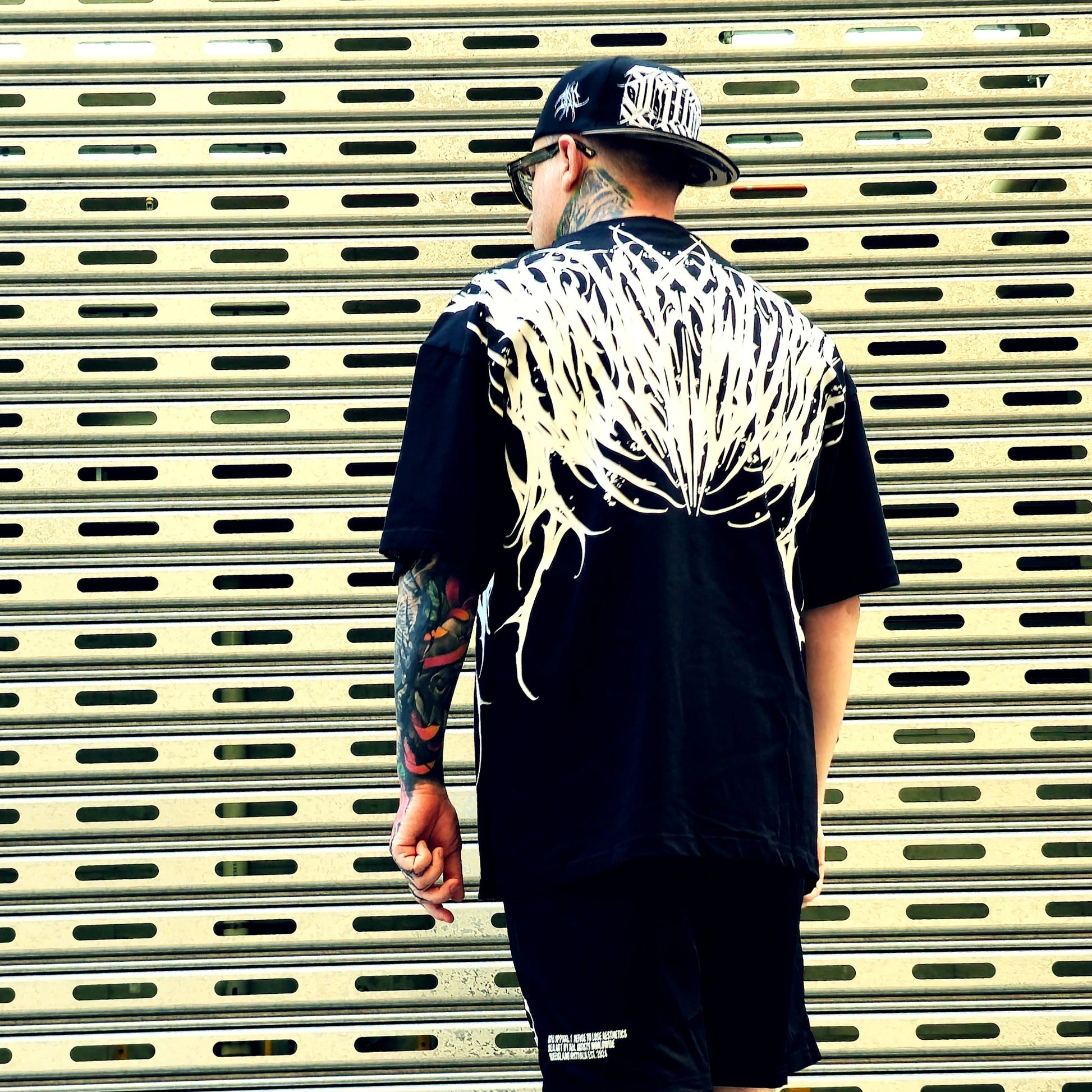 Person wearing a black t-shirt with white graphic design, standing in front of a metallic shutter.