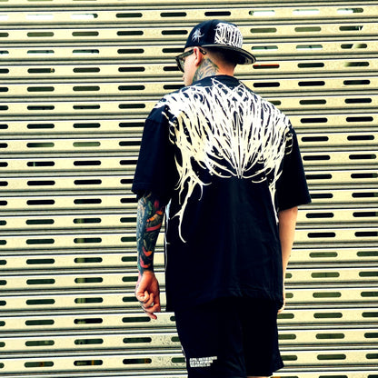 Person wearing a black t-shirt with white graphic design, standing in front of a metallic shutter.