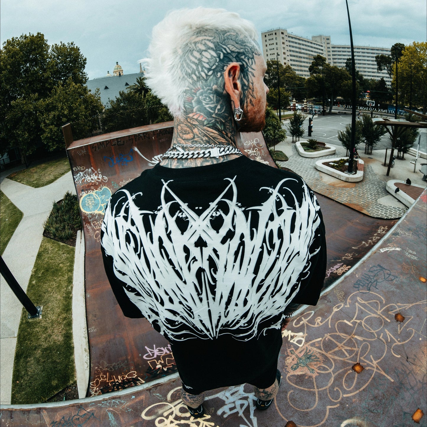 Person with extensive tattoos on a skate park with graffiti and urban elements.